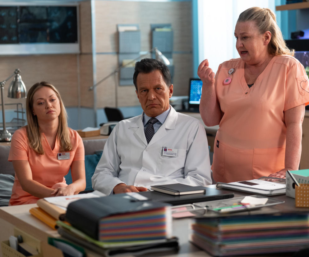 Trzyosobowa scena z serialu Na dobre i na złe, gdzie aktorzy Tomasz Ciachorowski jako Maks Beger, Anna Głosek jako Martyna oraz Aleksandra Grabowska jako Gloria dyskutują. Beger siedzi przy biurku, Martyna obok niego, a Gloria stoi. Więcej o Super Seriale przeczytasz na naszym portalu.