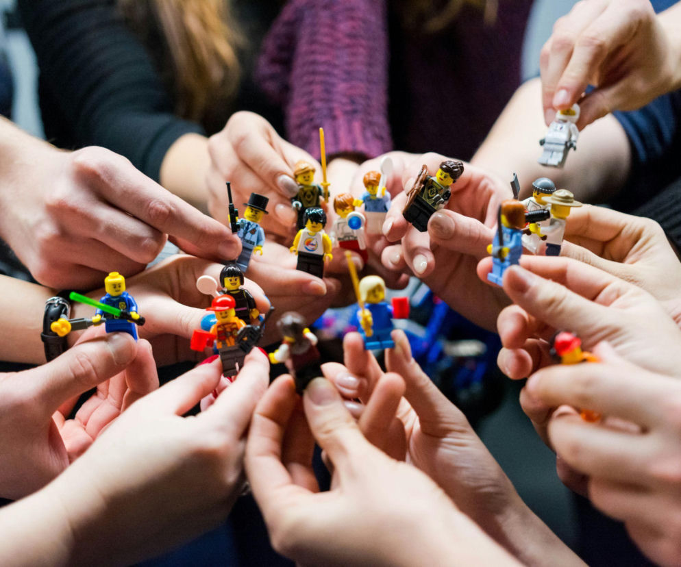 Dłonie wielu osób trzymających różne figurki LEGO. O nowej współpracy LEGO i Sanrio przeczytasz na SE.