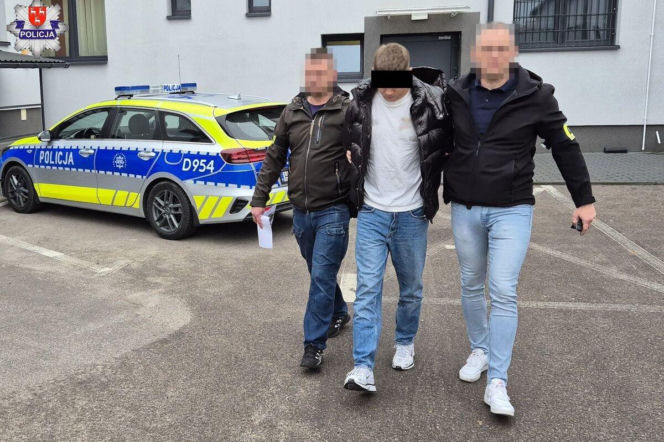 Policjanci prowadzą zatrzymanego 20-latka obok radiowozu. O oszustwach w regionie przeczytasz na Eska Siedlce.