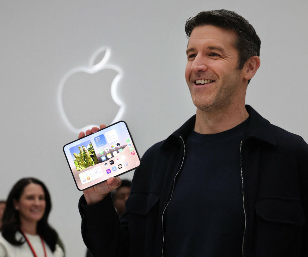 Uśmiechnięty John Ternus prezentuje iPhone'a Duo na tle logo Apple. O rewolucji w technologii przeczytasz na Eska.