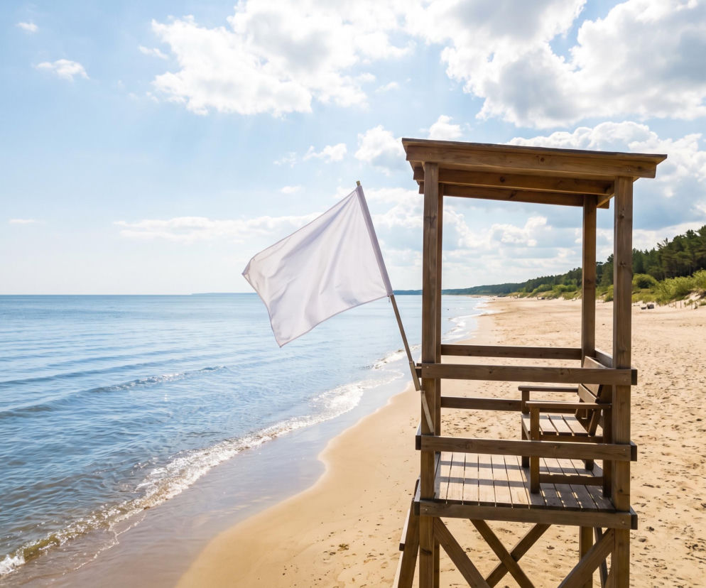 Biała flaga na wieży ratowniczej przy pustej plaży w Pogorzelicy. O warunkach nad morzem przeczytasz na SE Szczecin.