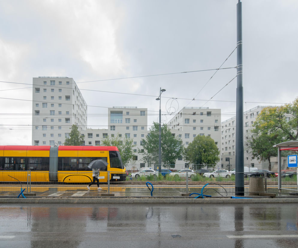Nowoczesny budynek TBS na Ochocie w deszczowy dzień. Przed nim przejeżdża żółty tramwaj. O inwestycji przeczytasz na Architektura.