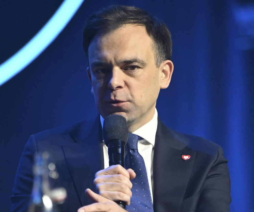 Andrzej Domański, minister finansów, w garniturze i krawacie, podczas wystąpienia publicznego, z mikrofonem w dłoni. Omówienie planów rządu wobec cen paliw i podatku windfall tax można przeczytać na Super Biznes.