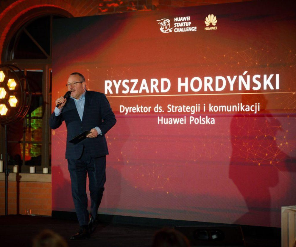 Ryszard Hordyński, Dyrektor ds. Strategii i Komunikacji Huawei Polska, przemawiający z mikrofonem na scenie podczas Huawei Startup Challenge V. Na tle ekran z logo konkursu. O szczegółach konkursu przeczytasz na Super Biznes.