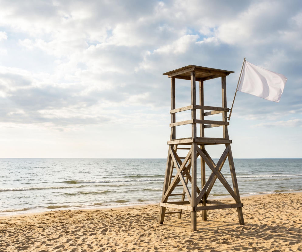Drewniana wieża ratownika z białą flagą na plaży w Trzęsaczu. O bezpiecznej kąpieli przeczytasz na SE Szczecin.