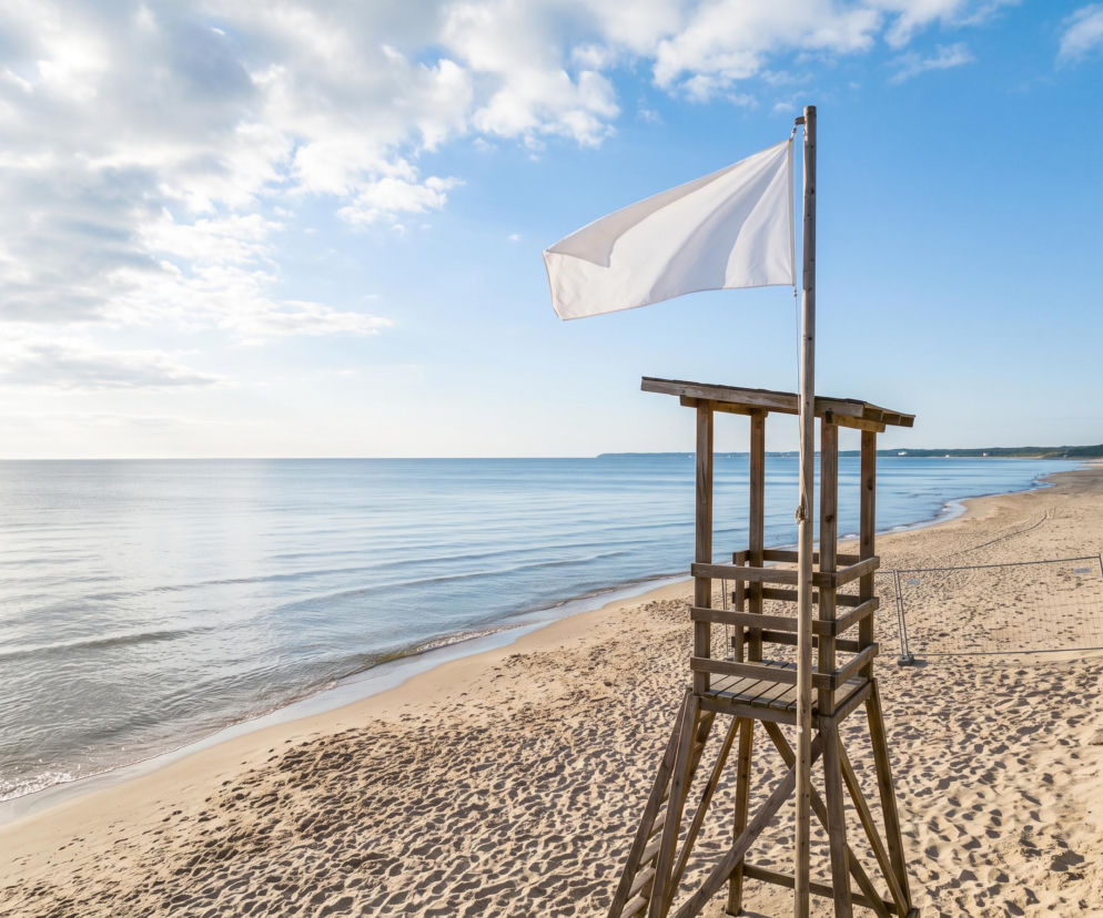 Drewniana wieża ratownika z białą flagą na pustej, piaszczystej plaży. O pogodzie w Świnoujściu przeczytasz na SE Szczecin.
