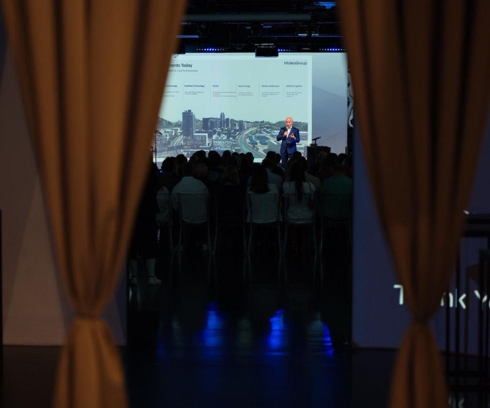 Uczestnicy wydarzenia Midea Group oglądający prezentację na dużym ekranie, na którym widać panoramę miasta i prelegenta. To kluczowy moment eventu, relacja z którego dostępna jest na naszym portalu.