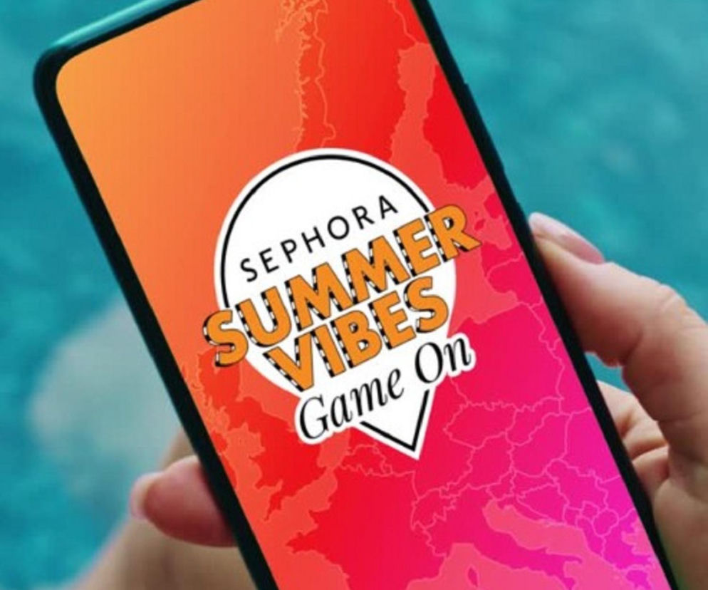 Smartfon z widoczną na ekranie grafiką gry Sephora Summer Vibes Game On na tle turkusowej wody basenu. Dłoń trzymająca telefon, odzwierciedla letni, beztroski nastrój, symbolizujący interaktywną rozrywkę i szansę na zdobycie nagród, o której przeczytasz na naszym portalu.