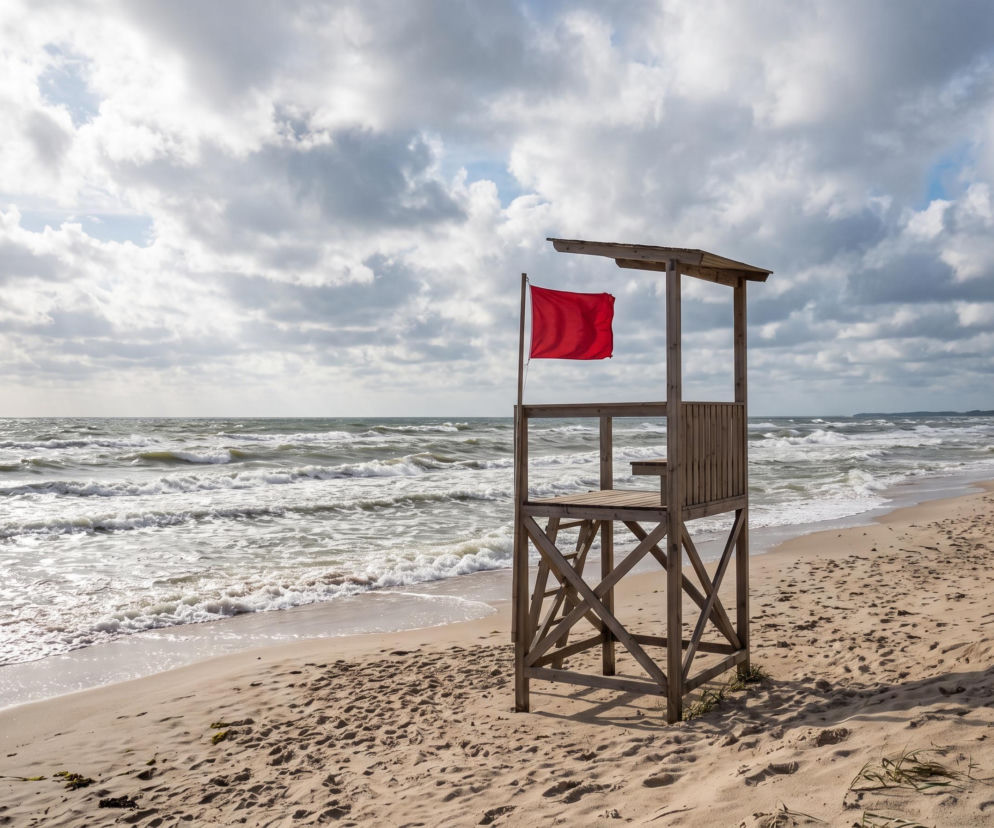 Drewniana wieża ratownicza z czerwoną flagą na plaży w Pobierowie. O zakazie kąpieli przeczytasz na SE Szczecin.