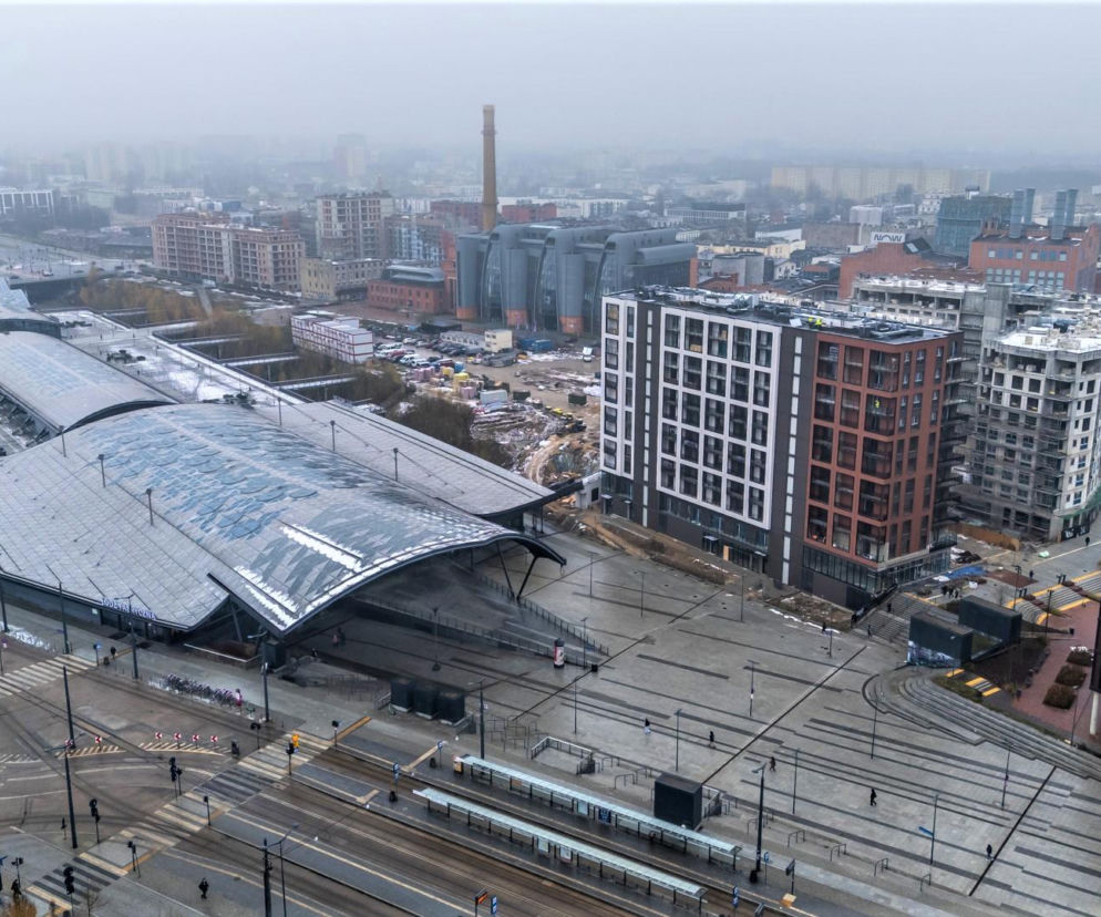 Panorama osiedla Flow w Łodzi, widoczna z góry. Ukazuje nowoczesne budynki mieszkalne z elewacjami w odcieniach brązu, szarości i bieli, nawiązujące do łódzkich kamienic. W tle Dworzec Łódź Fabryczna z charakterystycznym dachem. Architektura Murator Plus opisuje transformację Łodzi.