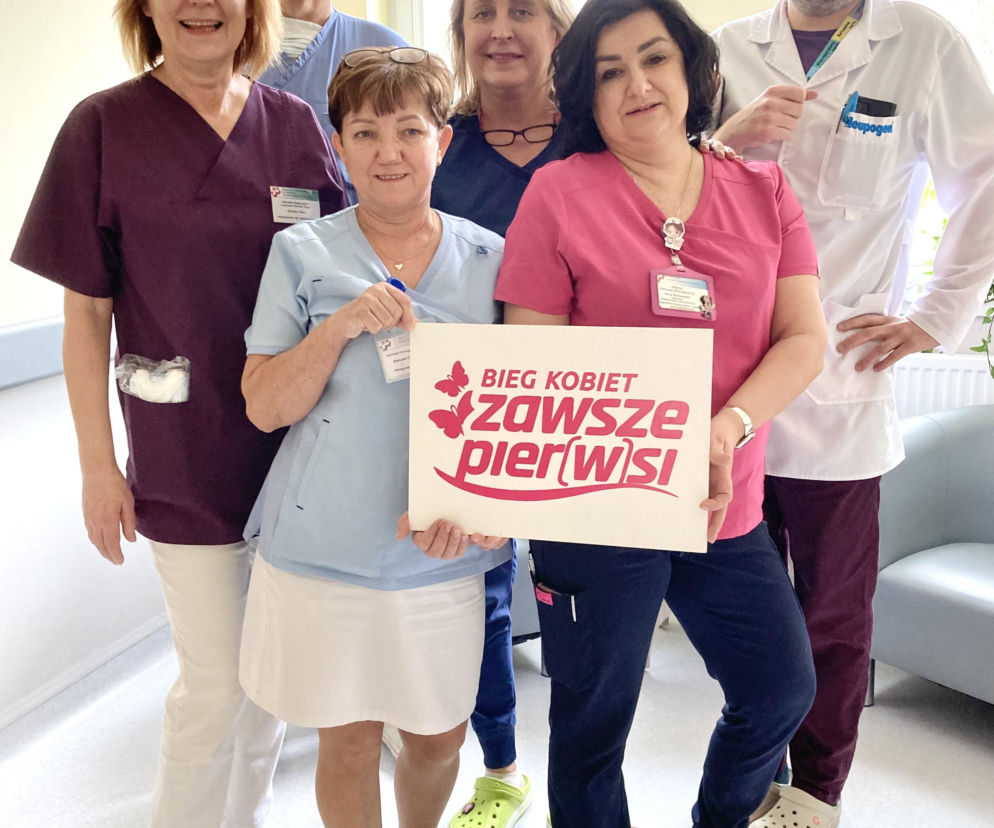 Grupa lekarzy i pielęgniarek trzymająca plakat Bieg Kobiet Zawsze Pier(w)si w celu promocji profilaktyki raka szyjki macicy. Możesz przeczytać o tym więcej na portalu Poradnik Zdrowie.