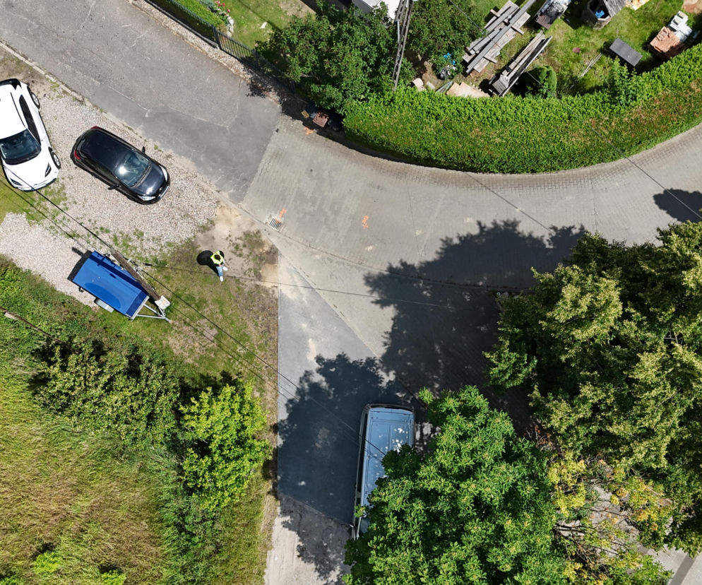 Widok z lotu ptaka na skrzyżowanie ulicy Korsaka w Gorzowie, z widocznym pracownikiem w kamizelce odblaskowej nadzorującym prace drogowe. Obok niego zaparkowane samochody oraz fragment przyczepy. Cały artykuł o inwestycjach drogowych i utrudnieniach w ruchu przeczytasz na naszym portalu.