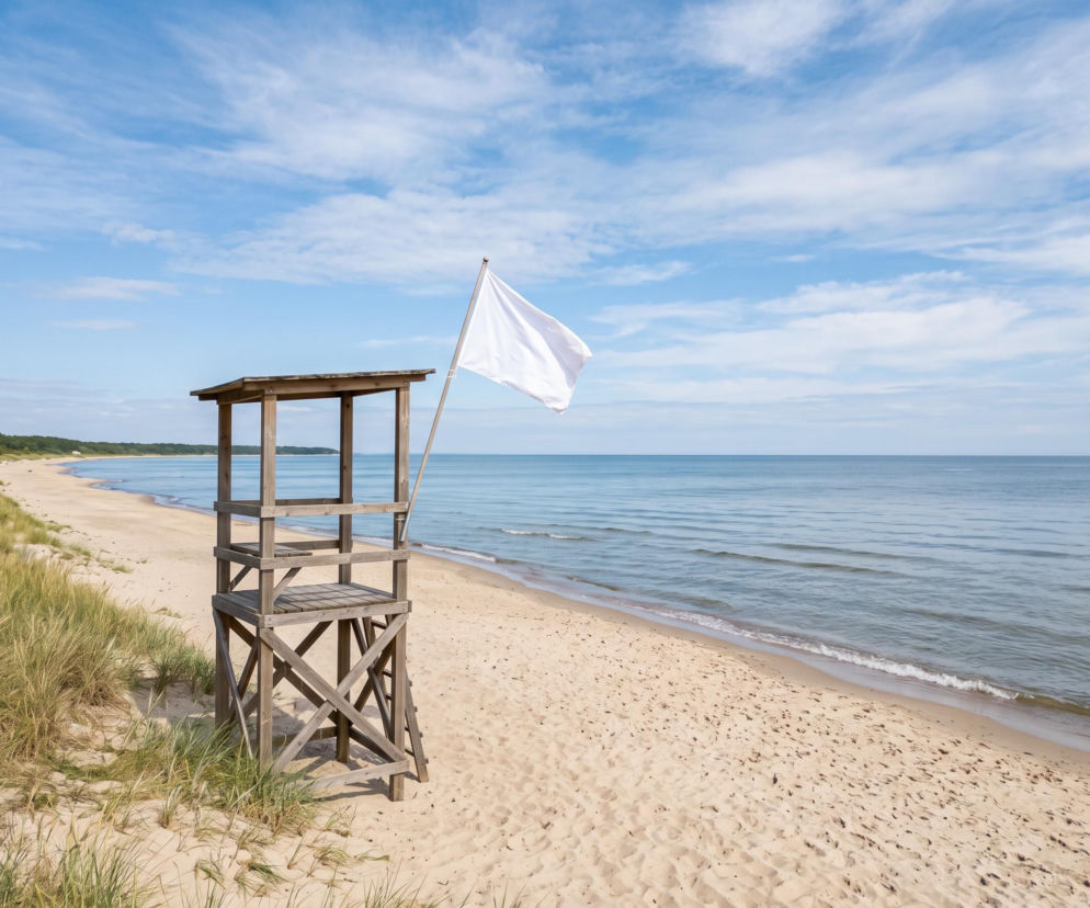 Drewniana wieża ratownicza na piaszczystej plaży z białą flagą. O bezpieczeństwie w Łazach dowiesz się z SE Szczecin.