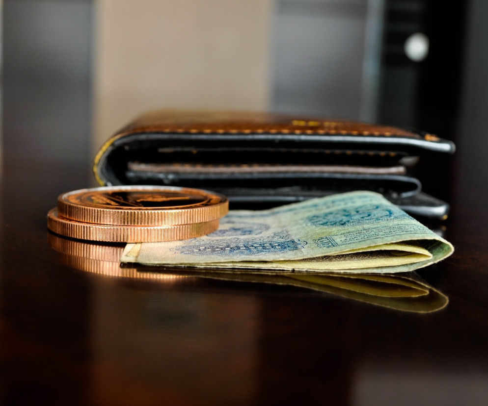 Portfel, plik banknotów i stos monet na ciemnym, lśniącym blacie, symbolizujące oszczędności w PPK, o których przeczytasz więcej na portalu Super Biznes.
