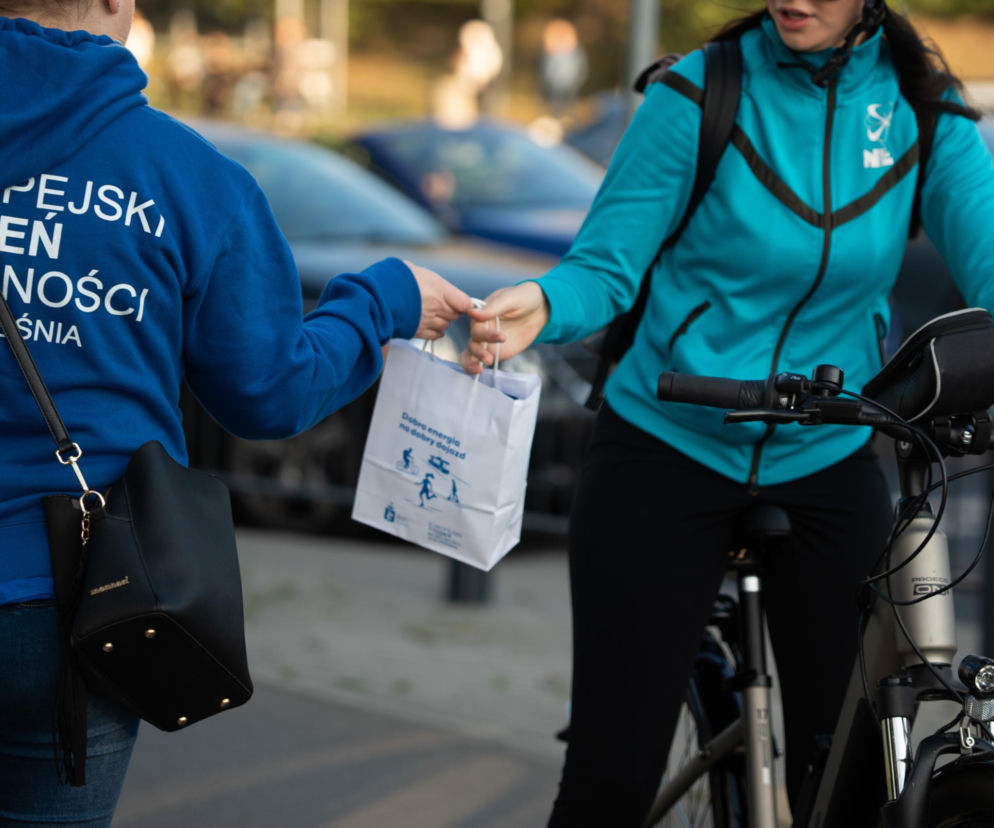 Osoba w bluzie z napisem Europejski Tydzień Mobilności podaje torebkę rowerzystce. O akcji w Warszawie przeczytasz na SE.