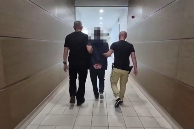 Dwaj policjanci prowadzą zakutego w kajdanki mężczyznę korytarzem. O zatrzymaniu gwałciciela z Piły przeczytasz na SE.