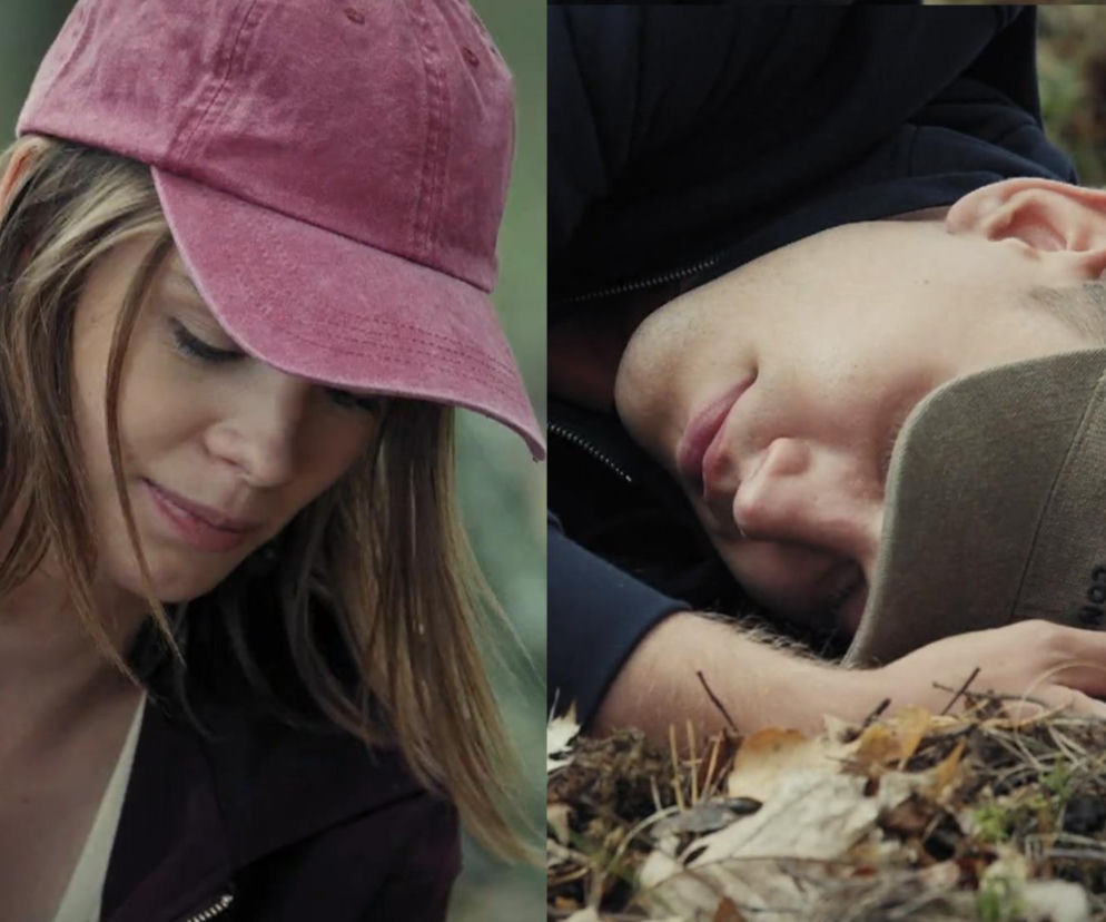 Majka w różowej czapce patrzy z niepokojem, podczas gdy nieprzytomny Mateusz leży na ziemi w zielonej czapce po wypadku rowerowym. Scena z M jak miłość ilustruje dramatyczne wydarzenia, o których przeczytasz więcej na Super Seriale.