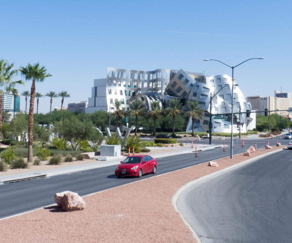 Charakterystyczna, falująca bryła Lou Ruvo Center for Brain Health w Las Vegas projektu Franka Gehry'ego, z elewacją z 18 tysięcy stalowych płytek. Widok na budynek z ulicy, z palmami i czerwonym samochodem. Więcej o tym projekcie na Architektura Murator Plus.