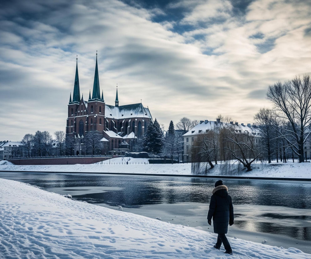 Na pierwszym planie, z prawej strony, człowiek w ciemnej zimowej kurtce z futrzanym kapturem oraz ciemnych spodniach i rękawiczkach idzie po śniegu wzdłuż rzeki. Długa kurtka sięga do kolan, a na głowie ma czapkę. Brzeg rzeki, po którym idzie, jest całkowicie pokryty białym, puszystym śniegiem, na którym widać liczne ślady stóp. Rzeka zajmuje środek kadru, jej ciemne wody odbijają światło, tworząc jasne refleksy, a fragmenty jej powierzchni są częściowo zamarznięte. Na lewym brzegu rzeki, w oddali, widać most oraz rząd zaśnieżonych drzew. W tle dominuje duży, ceglany kościół z dwiema wysokimi, spiczastymi wieżami pokrytymi zielonkawym dachem oraz mniejszą wieżyczką, również przysypany śniegiem. Niebo jest pochmurne, z widocznymi warstwami białych i szarych chmur, które gdzieniegdzie prześwitują na niebiesko, a w prawej części kadru widać jaśniejsze, rozproszone światło.