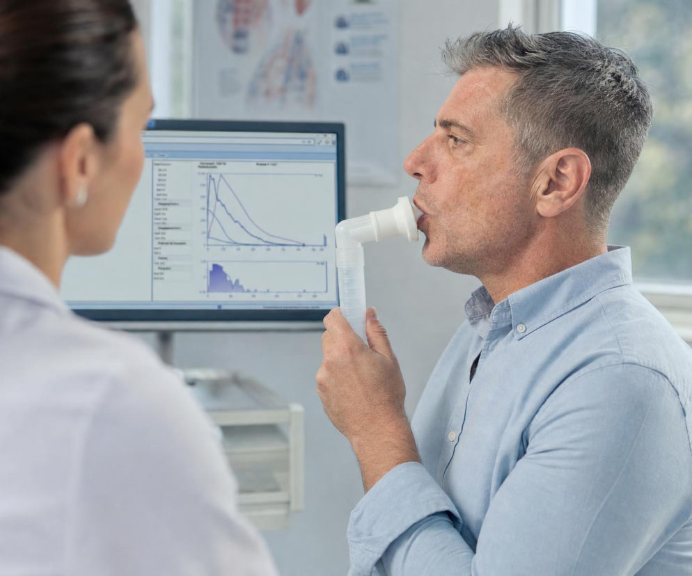 Mężczyzna wykonuje badanie spirometryczne płuc w gabinecie. O przebiegu badania przeczytasz na Poradnik Zdrowie.