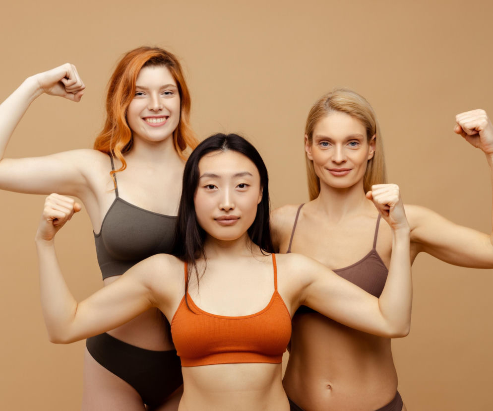 Trzy kobiety w bieliźnie napinają bicepsy, prezentując zdrową skórę. O idei skin fitness przeczytasz na SE.