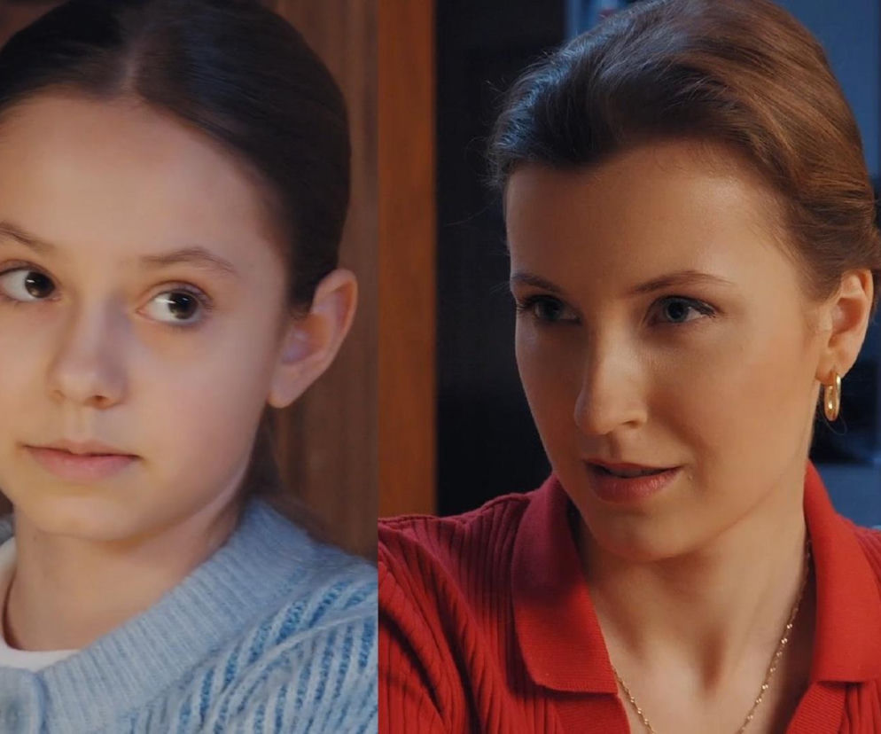 Hania (Wiktoria Basik) w jasnoniebieskim swetrze patrzy w prawo, obok niej Natalka (Dominika Suchecka) w czerwonej bluzce polo, uśmiecha się, patrząc na Hannę. Scena z serialu „M jak miłość”, w którym Hania odkrywa powody przekładania ślubu przez Natalkę. Więcej na Super Seriale.