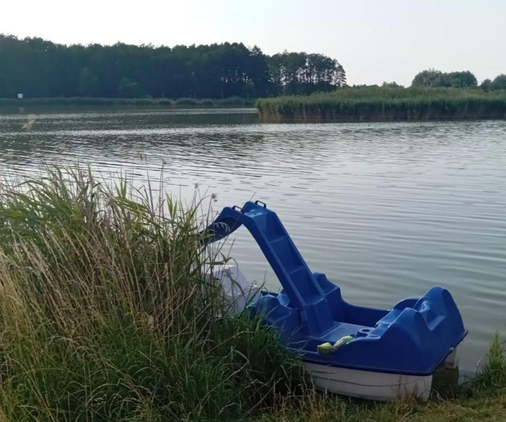 Niebieski rower wodny przy brzegu zarośniętego trzcinami zalewu, symbolizujący tragiczną śmierć 22-latka w Zamościu. Więcej o utonięciach nad wodą w regionie przeczytasz na naszym portalu.