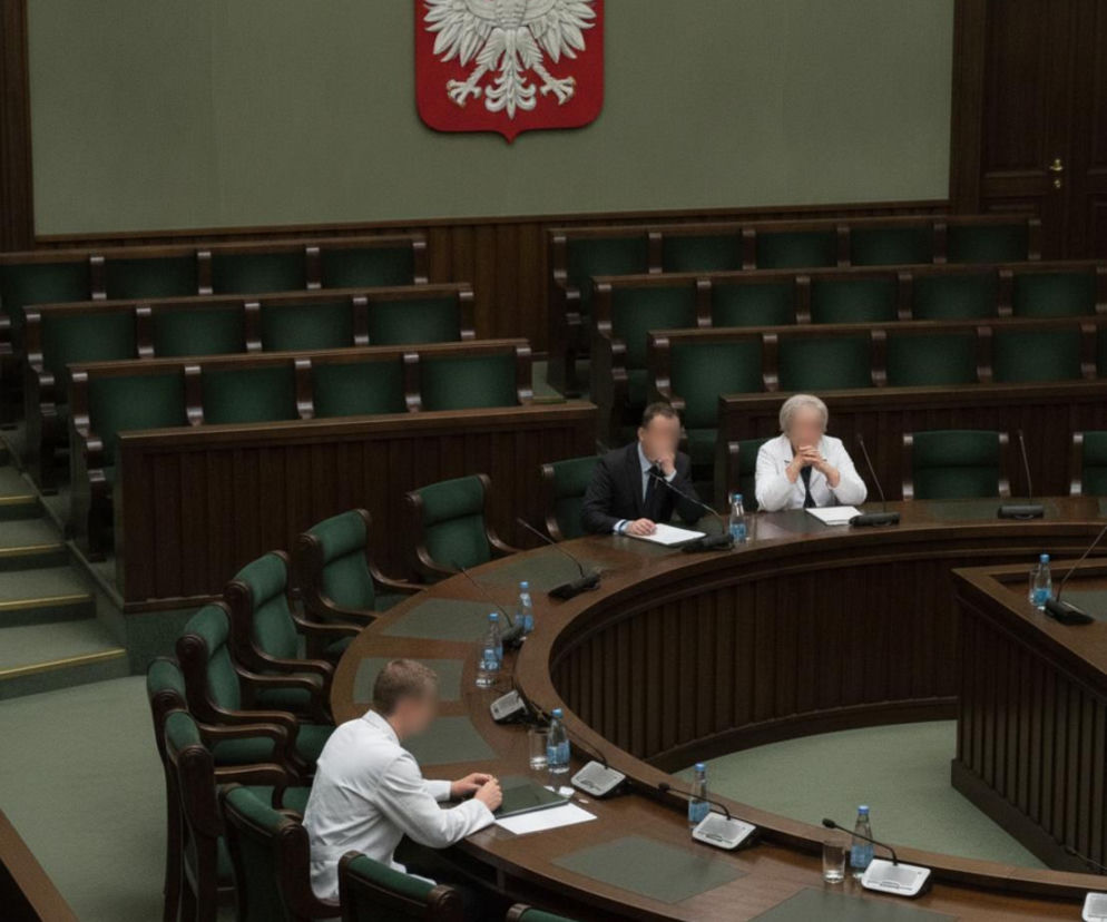 Lekarze i urzędnik przy stole w sali obrad Sejmu RP pod godłem Polski. O narodowej debacie o zdrowiu przeczytasz na PZ.
