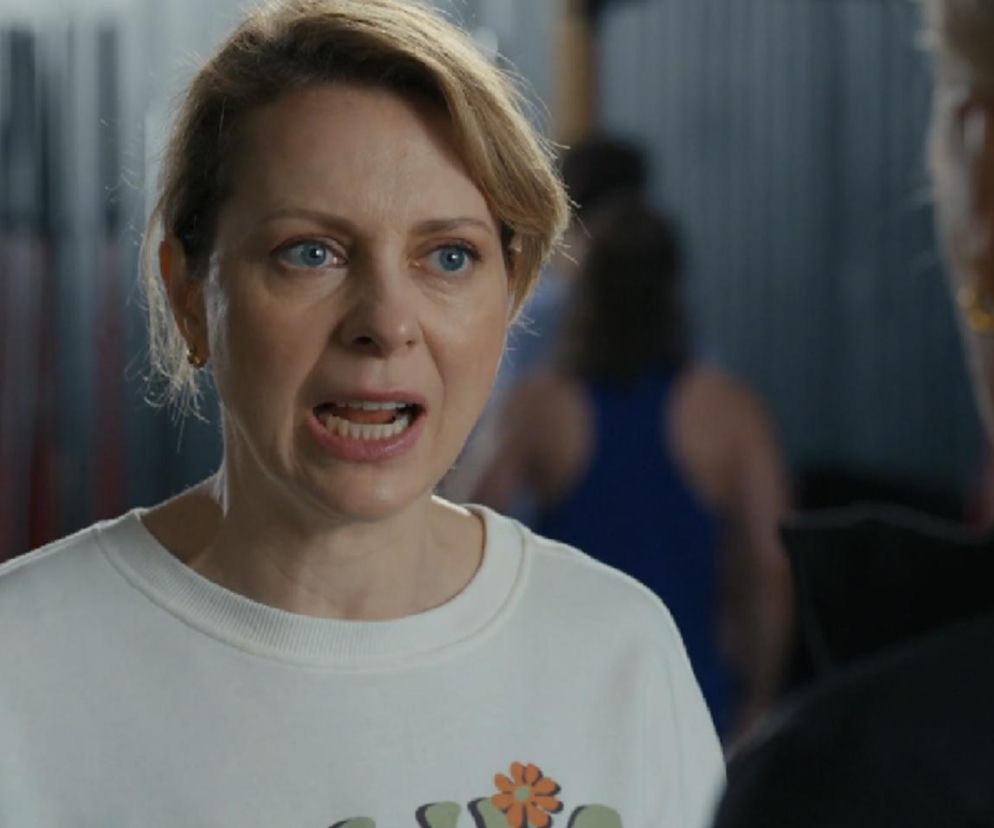 Kobieta z krótkimi, blond włosami, Dorota Kujawiak (Karina Seweryn) z serialu „Barwy szczęścia”, w białej bluzie, z otwartymi ustami, wyraża gniew w kierunku innej kobiety, widocznej od tyłu. Scena z siłowni, gdzie dochodzi do awantury Kujawiak z Justyną (Sylwia Juszczak-Krawczyk). Więcej o odcinkach serialu przeczytasz na Super Seriale.