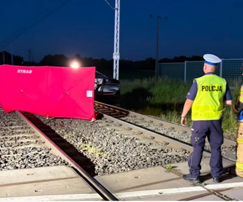 Widok na miejsce śmiertelnego wypadku w Nekli, gdzie doszło do zderzenia auta z drezyną. Czerwona plandeka przykrywa ofiarę na torach, obok widać uszkodzony samochód i służby ratunkowe. O tej tragedii możesz przeczytać więcej na naszym portalu.