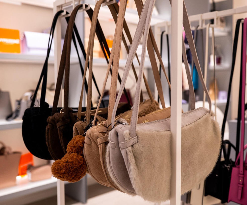 Jesienne torebki marki TOUS na białym stojaku w butiku. O trendach w dodatkach przeczytasz na SE.