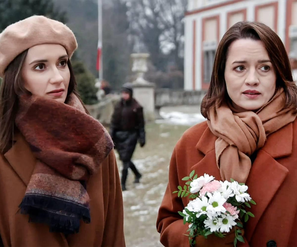 Melka (Ewa Jakubowicz) w beżowym berecie i Laura (Katarzyna Maciąg) z bukietem kwiatów, obie w płaszczach, spoglądają zaniepokojone w scenerii zimowego ogrodu, gdzie w tle majaczy pałac. Zdjęcie ilustruje odcinek serialu Pierwsza miłość, o którym więcej przeczytasz na Super Seriale.