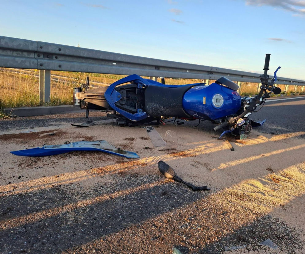 Rozbity niebieski motorower Junak leżący na asfalcie przy barierkach. O wypadku 17-latka przeczytasz w Eska Leszno.