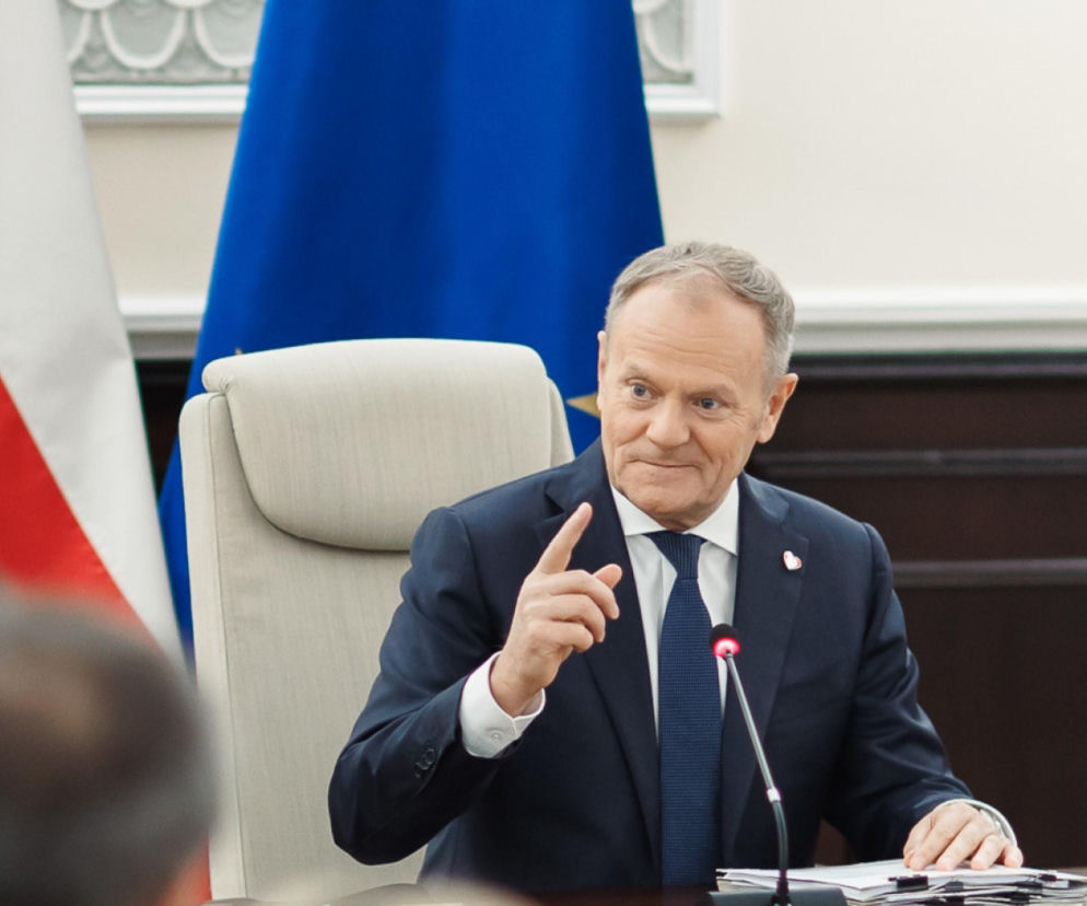 Donald Tusk, premier, podczas posiedzenia, w tle polska i unijna flaga. Premier Tusk nakazał wstrzymanie wielkiej reformy, o czym przeczytasz na portalu Super Biznes.