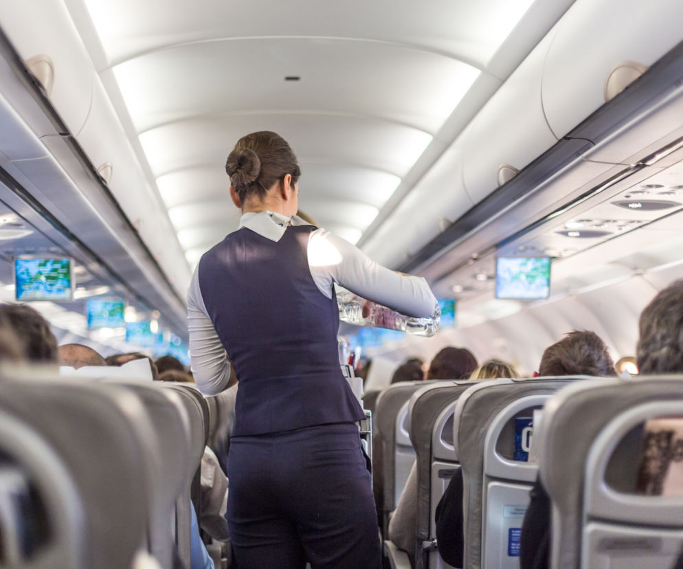 Stewardesa w mundurze serwująca napoje pasażerom w samolocie. Zdjęcie ilustruje temat kontroli trzeźwości personelu lotniczego na lotniskach, o których przeczytasz więcej na Super Biznes.