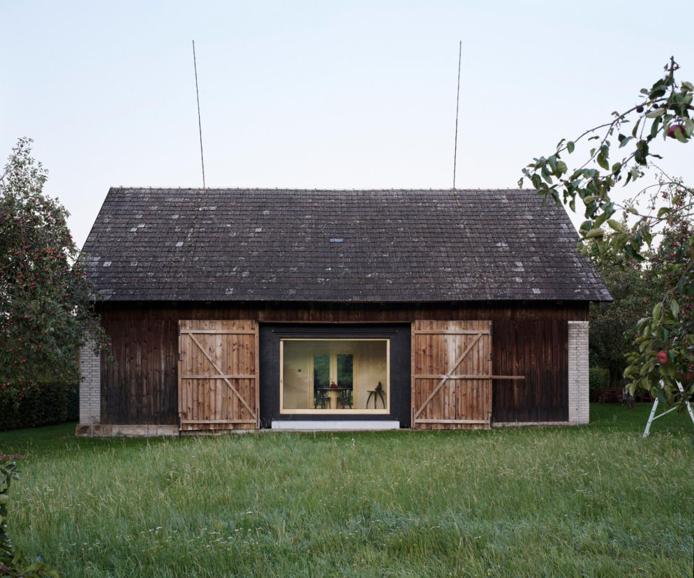 Historyczna drewniana stodoła z nowym panoramicznym oknem w czarnej ramie. O projekcie The Box in the Barn przeczytasz na Architektura.
