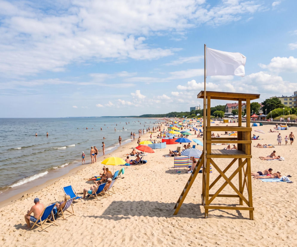 Słoneczna plaża w Mielnie z białą flagą na wieży ratowniczej. O bezpiecznych kąpielach przeczytasz na SE Szczecin.