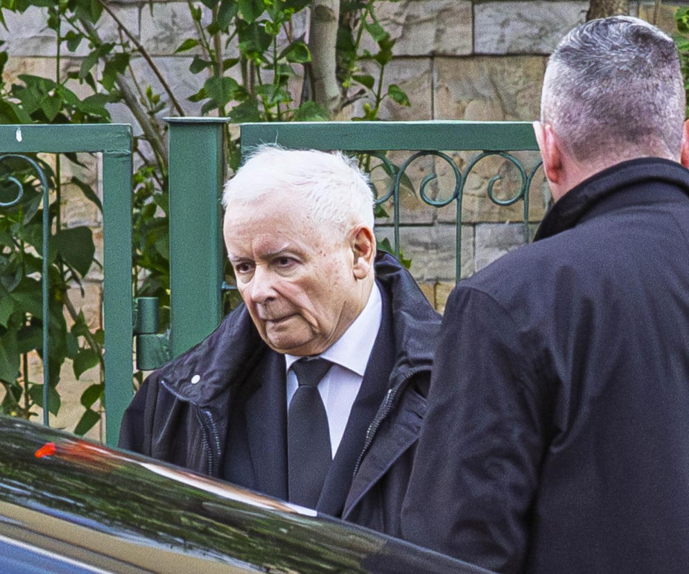 Prezes PiS Jarosław Kaczyński idzie obok ochroniarza przy zielonym ogrodzeniu. O procesie ochrony przeczytasz w VOX FM.