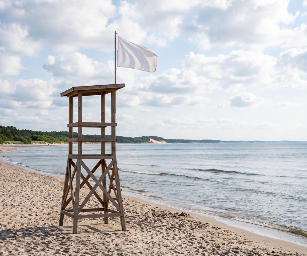 Drewniana wieża ratownicza z białą flagą na pustej plaży. O bezpieczeństwie kąpieli w Mielnie przeczytasz na SE Szczecin.