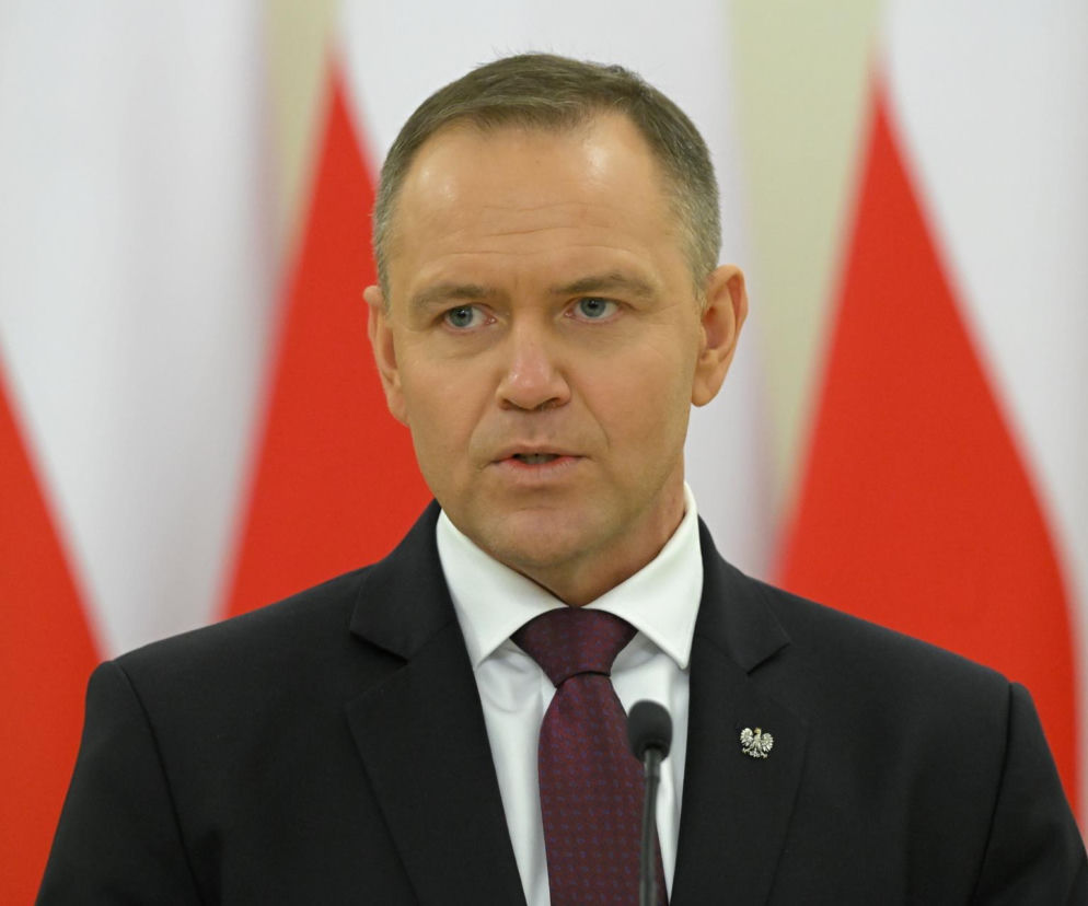 Prezydent Karol Nawrocki przemawiający na tle biało-czerwonych flag. Mężczyzna w garniturze i krawacie patrzy wprost, jego mina jest poważna. Tysiące firm czeka na jego decyzję ws. ustawy o cyberbezpieczeństwie, o której przeczytasz na Super Biznes.