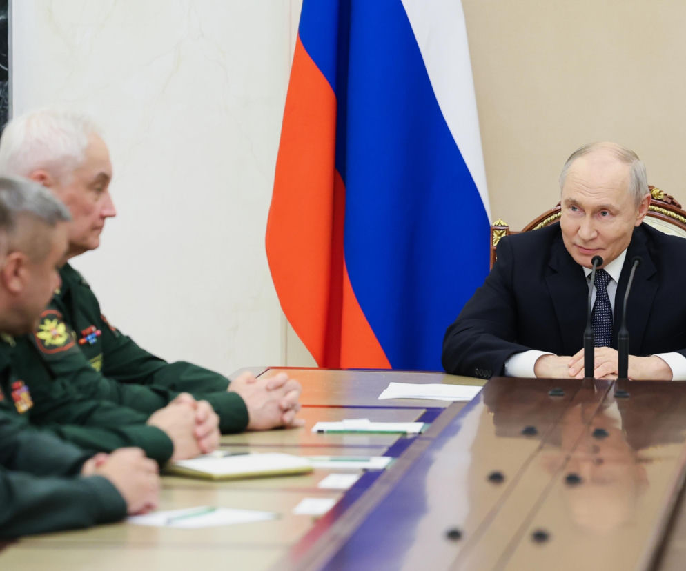 Władimir Putin siedzi przy stole naprzeciwko wojskowych na tle flagi Rosji. O jego planach na zimę przeczytasz na SE.