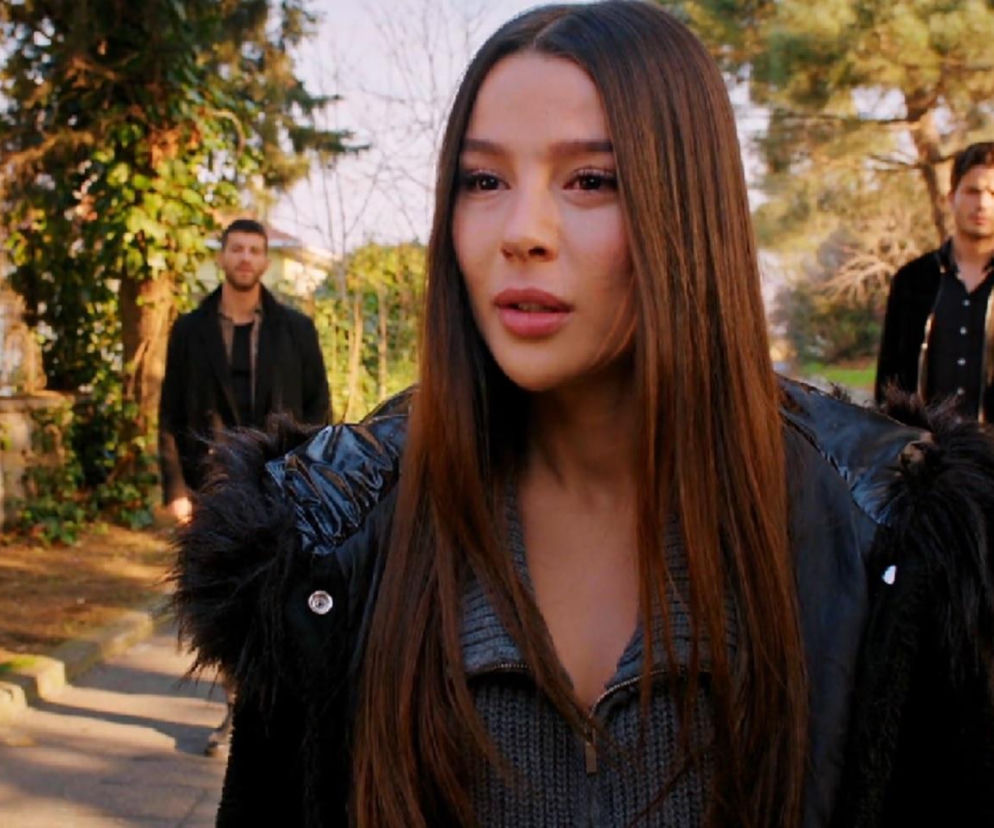 Zeynep, ubrana w czarną kurtkę z futrzanym kołnierzem, z długimi, brązowymi włosami, zamyślona, spogląda w dal. W tle, idąc za nią, widać Ege i Cihana. Ta scena z serialu Miłość i nadzieja symbolizuje trudny wybór Zeynep, co do którego można przeczytać więcej na portalu Super Seriale.