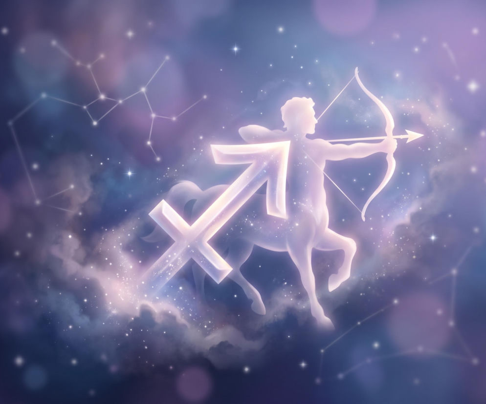 Świecący symbol zodiakalnego Strzelca na tle gwieździstego nieba i mgławic. O horoskopie przeczytasz w serwisie Eska.