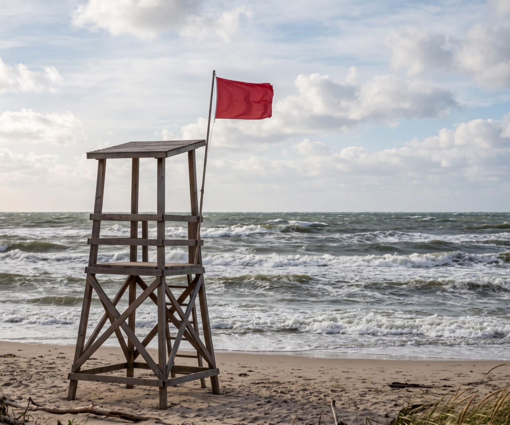 Drewniana wieża ratownicza z czerwoną flagą na plaży w Łazach. O zakazie kąpieli przeczytasz na SE Szczecin.