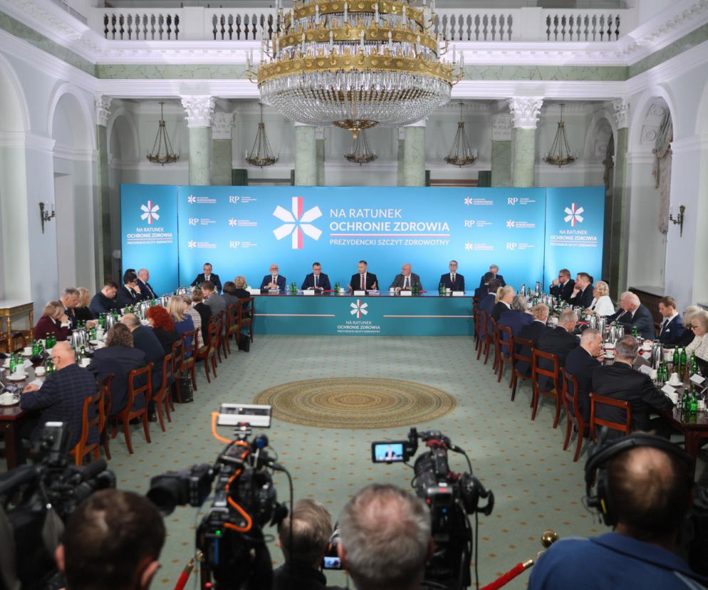 Prezydencki szczyt zdrowotny Na ratunek ochronie zdrowia z Karolem Nawrockim przy stole prezydialnym oraz licznie zgromadzonymi uczestnikami, w tym dziennikarzami, co widać po sprzęcie na pierwszym planie. Więcej o decyzjach w ochronie zdrowia przeczytasz na Poradnik Zdrowie.