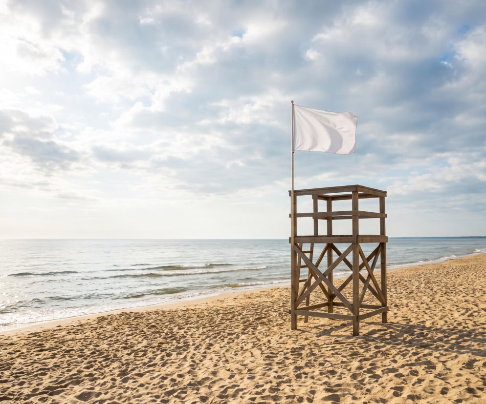 Drewniana wieża ratownicza z białą flagą na pustej plaży w Łazach. O warunkach nad morzem przeczytasz na SE Szczecin.