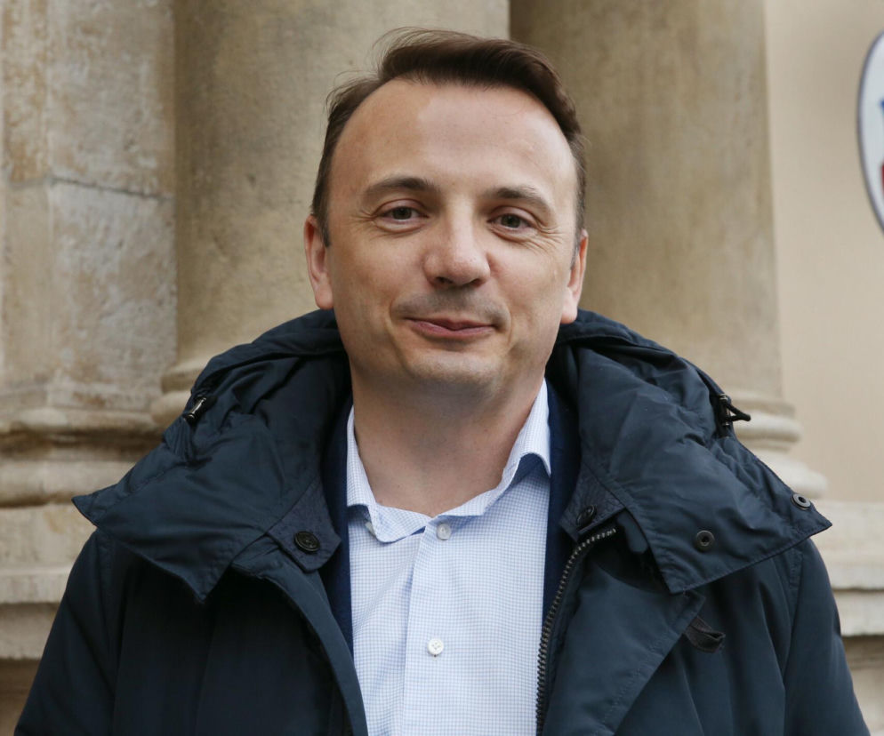 Łukasz Gibała w ciemnej kurtce na tle budynku. O planach kandydata na prezydenta Krakowa przeczytasz na SE Polityka.