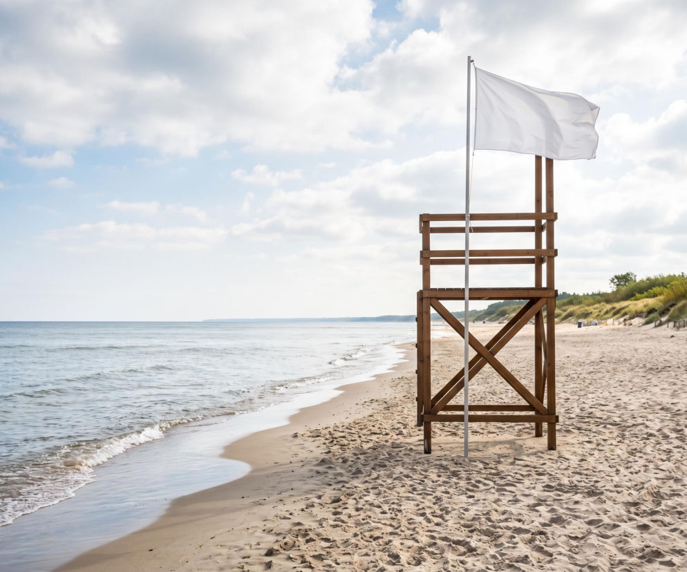 Drewniana wieża ratownika z powiewającą białą flagą na pustej plaży w Pobierowie. O pogodzie przeczytasz na SE Szczecin.