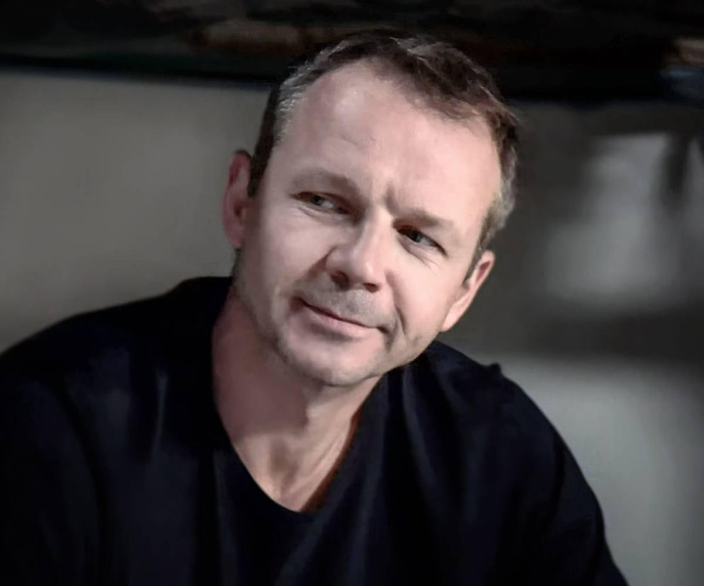 Zbliżenie na Mateusza Stika (Lesław Żurek) z serialu Pierwsza miłość, z mimiką wskazującą na podstęp. Mężczyzna ma krótkie, siwiejące włosy i ubrany jest w ciemną koszulkę. Zdjęcie ilustruje scenę, w której psychopatyczny Stik planuje ucieczkę z więzienia. Więcej o wątku Stika na Super Seriale.