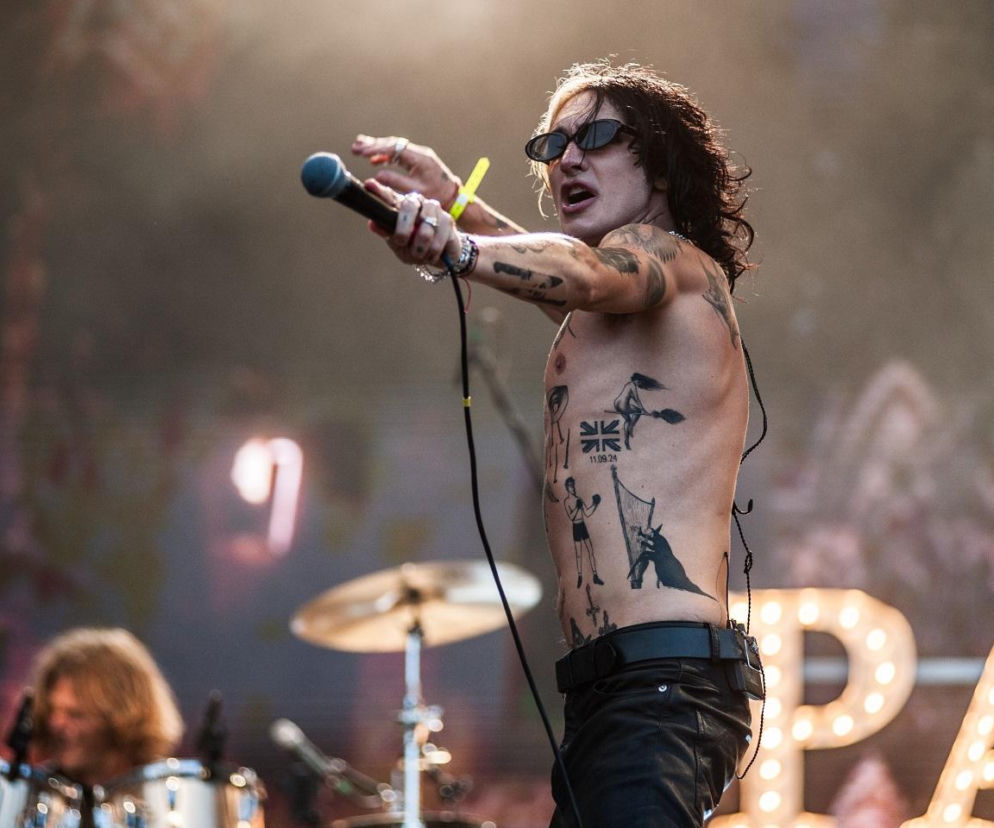 Wokalista Palaye Royale śpiewa do mikrofonu na koncercie. O trasie zespołu w Polsce przeczytasz na SE.